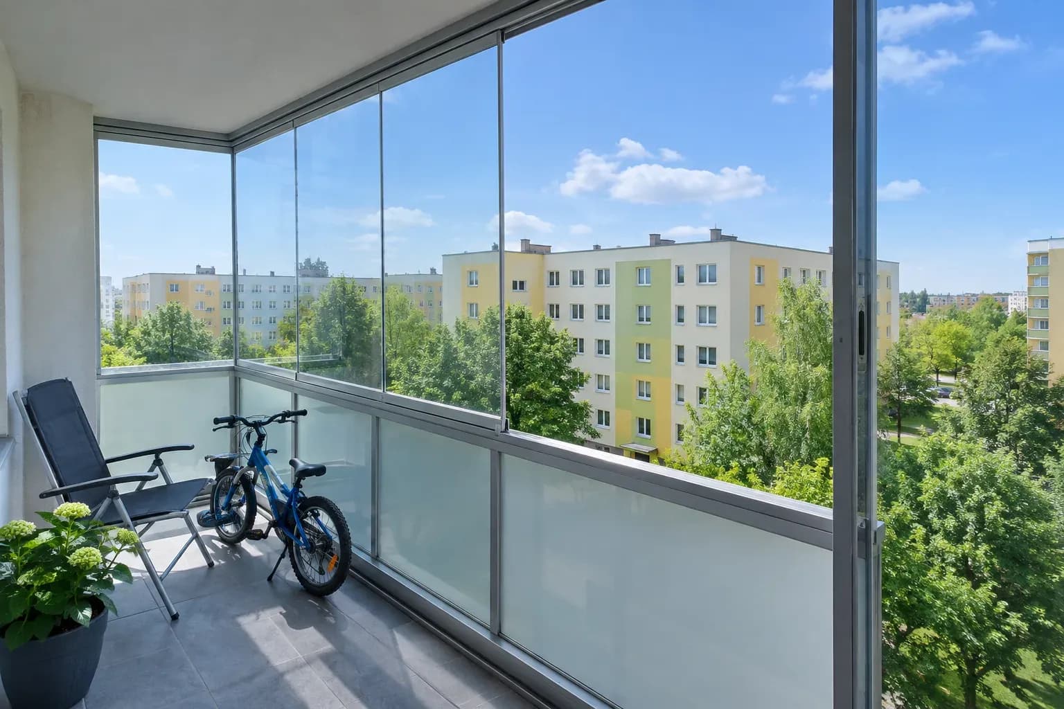 Balkon w bloku z przesuwanymi szybami, część otwarta, rower i krzesło w słoneczny dzień