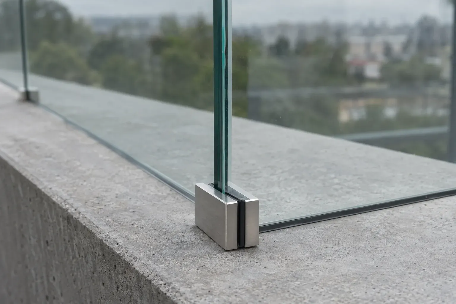Zbliżenie na narożnik szklanej balustrady bez ramy, zamocowanej przy krawędzi betonowej płyty balkonu